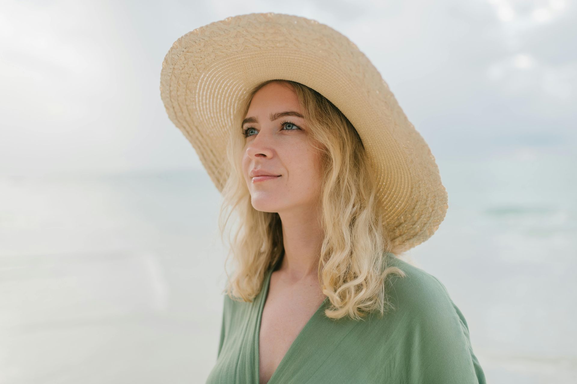 Blonde Frau mit Sonnenhut blickt zufrieden in die Ferne