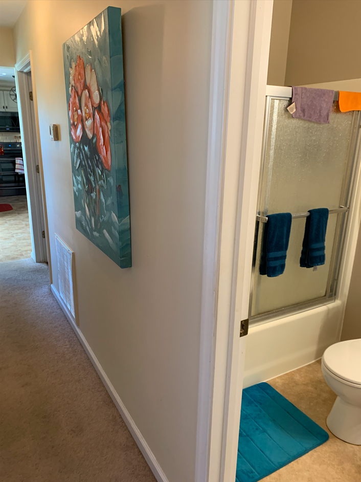 Hallway view into a bathroom with turquoise towels, rug, and wall art on a white wall
