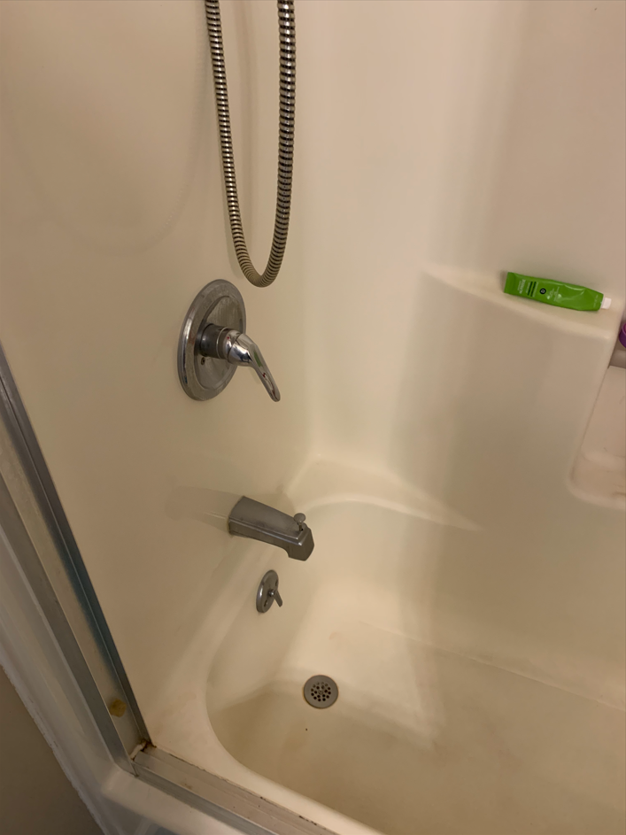 Bathtub shower area with chrome fixtures, beige walls, and a shampoo bottle on the tub ledge