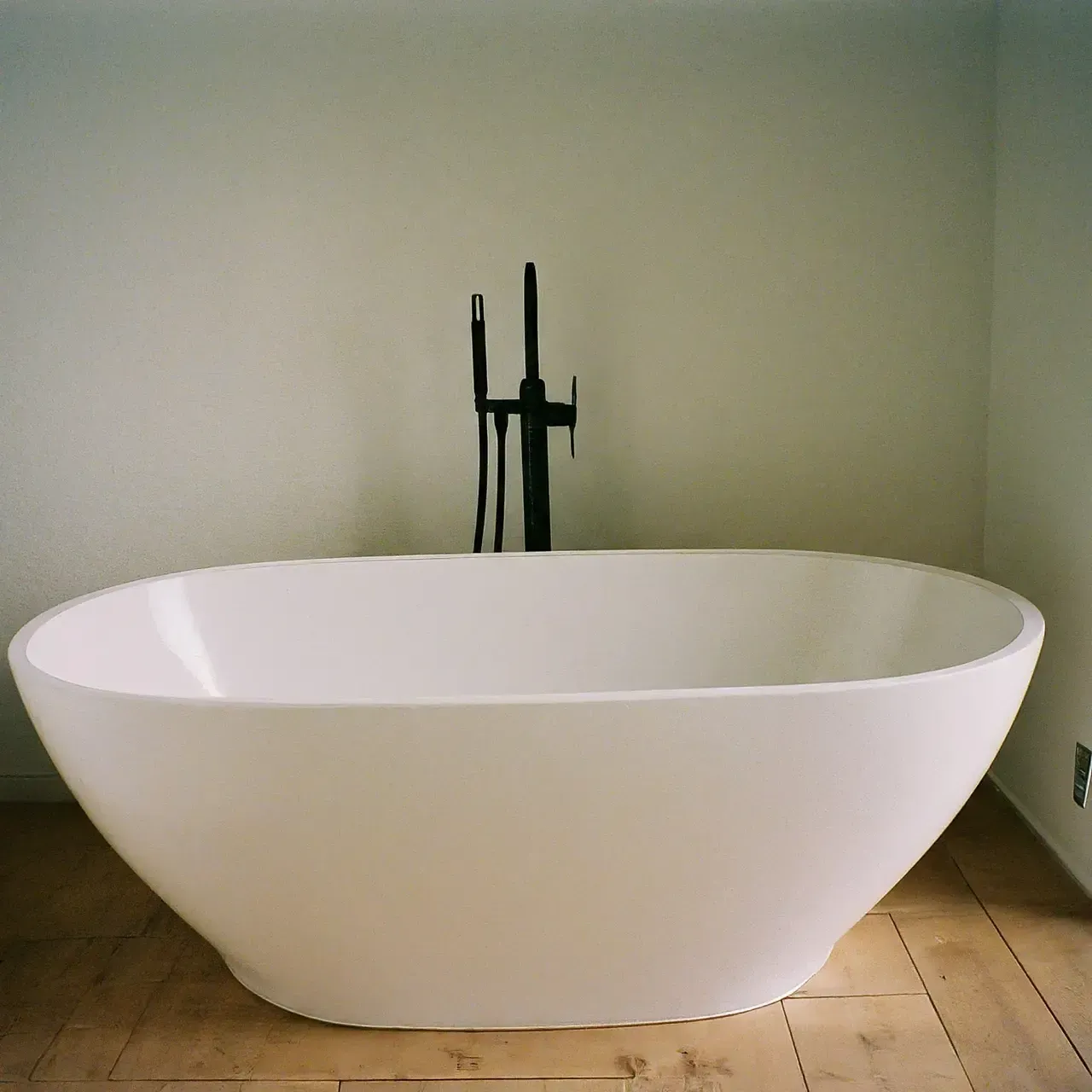 White freestanding bathtub in a minimalist bathroom with wood floor and black fixtures