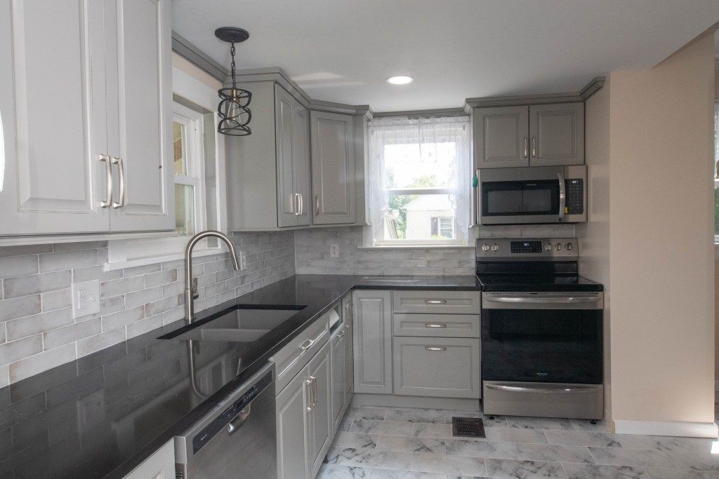 Modern gray kitchen with black countertops, stainless appliances, and a window over the sink