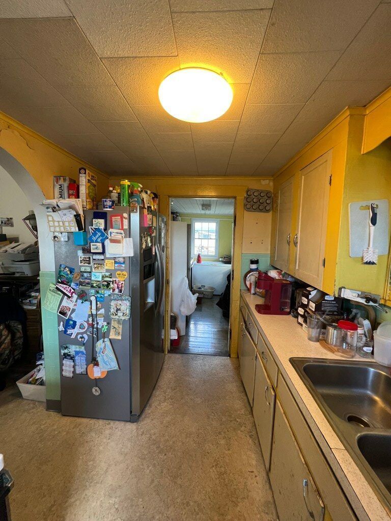 Small kitchen with yellow walls, fridge covered in magnets, and a sink and countertop on the right.