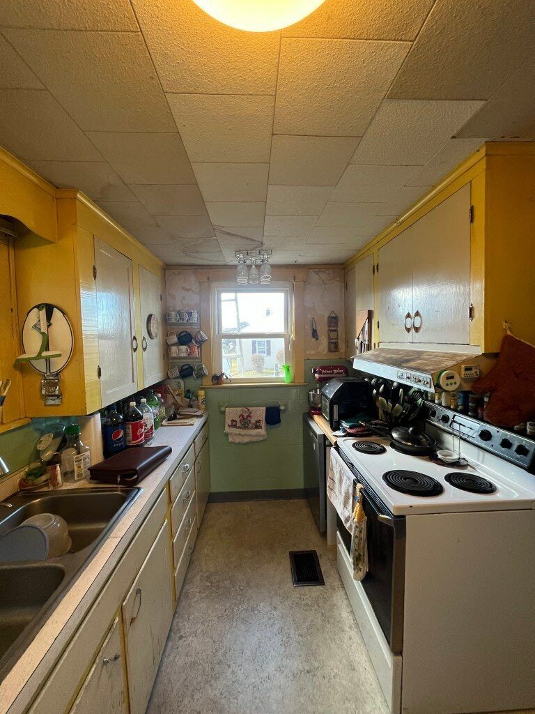 Narrow kitchen with yellow cabinets, white appliances, and a window at the far end.