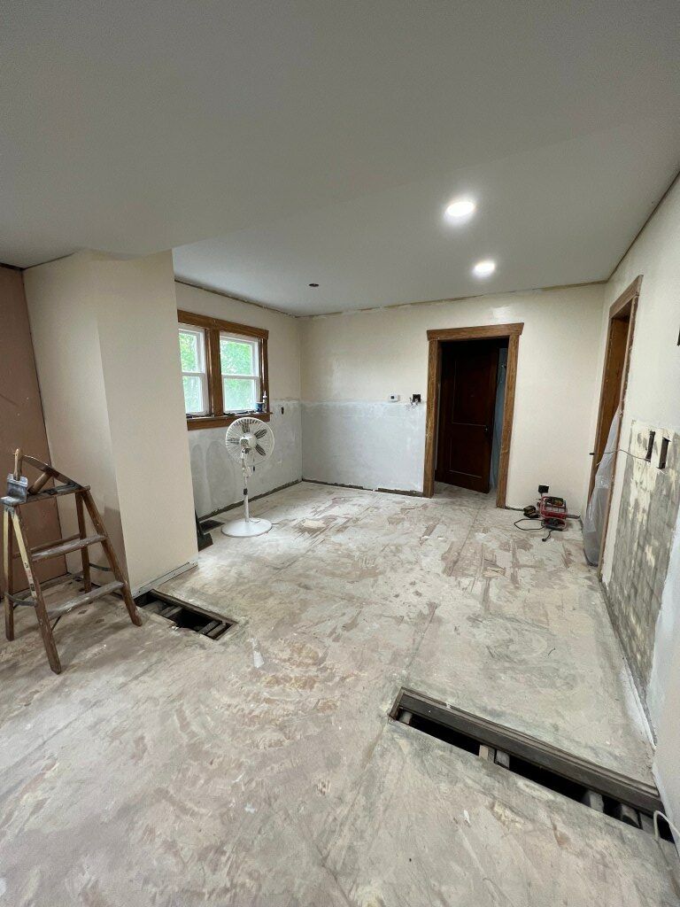 Renovation-ready room with bare walls, window, ladder, and floor cutouts for utilities