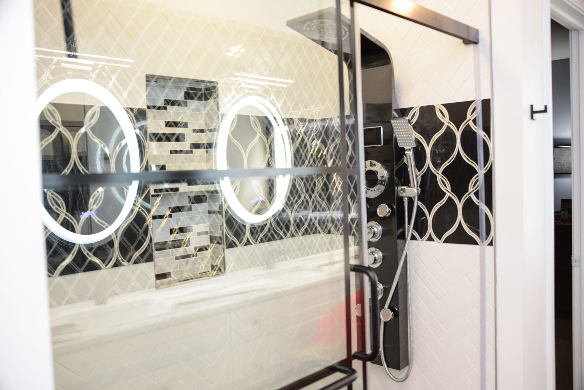 Modern bathroom with glass shower enclosure, black fixtures, and circular mirror accents