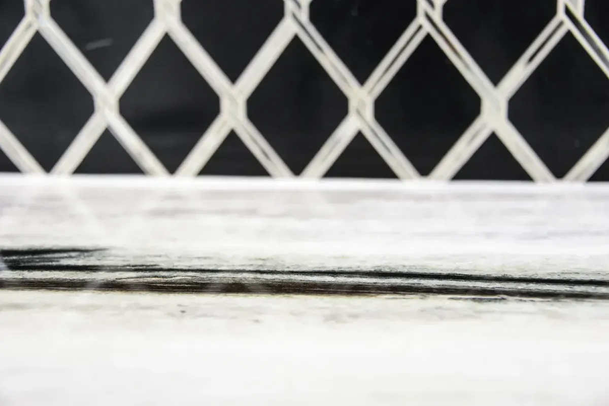 White diamond lattice fence above a weathered white ledge against a dark background