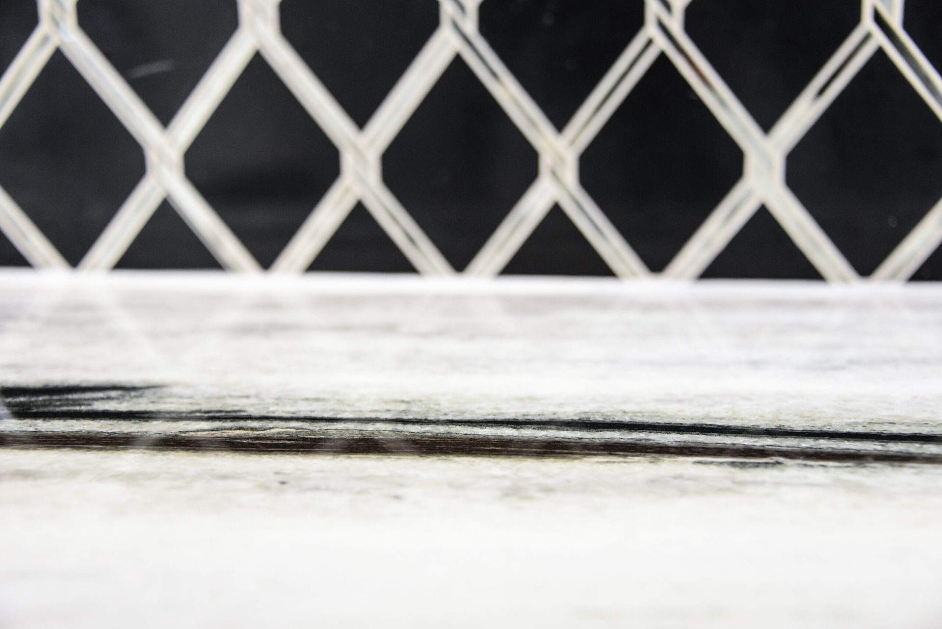 White metal lattice fence behind a dusty window ledge with dark smudges near the bottom.