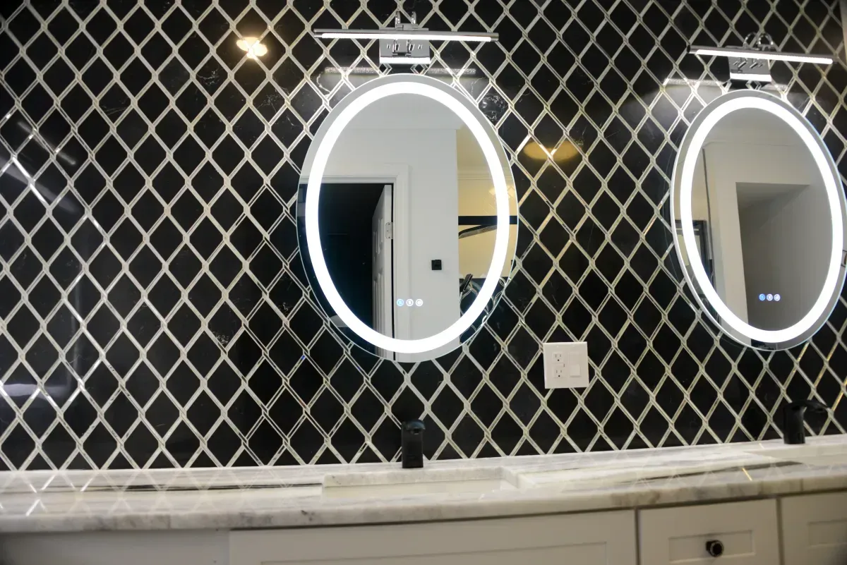 Bathroom vanity with two illuminated oval mirrors and black diamond-pattern tile wall