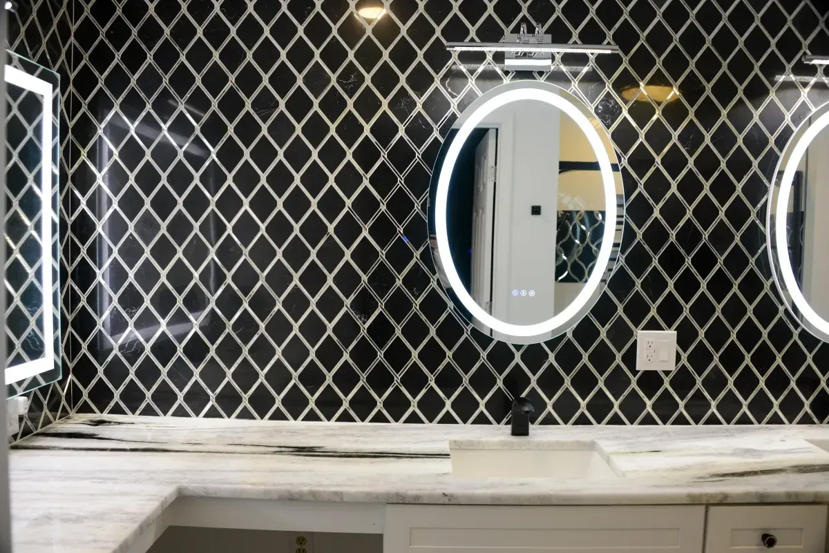 Bathroom vanity with a marble countertop, patterned wall, and oval backlit mirrors