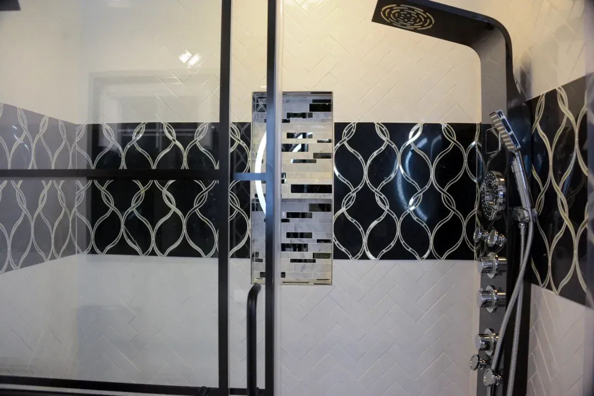 Modern shower stall with frosted glass doors and black patterned tile walls
