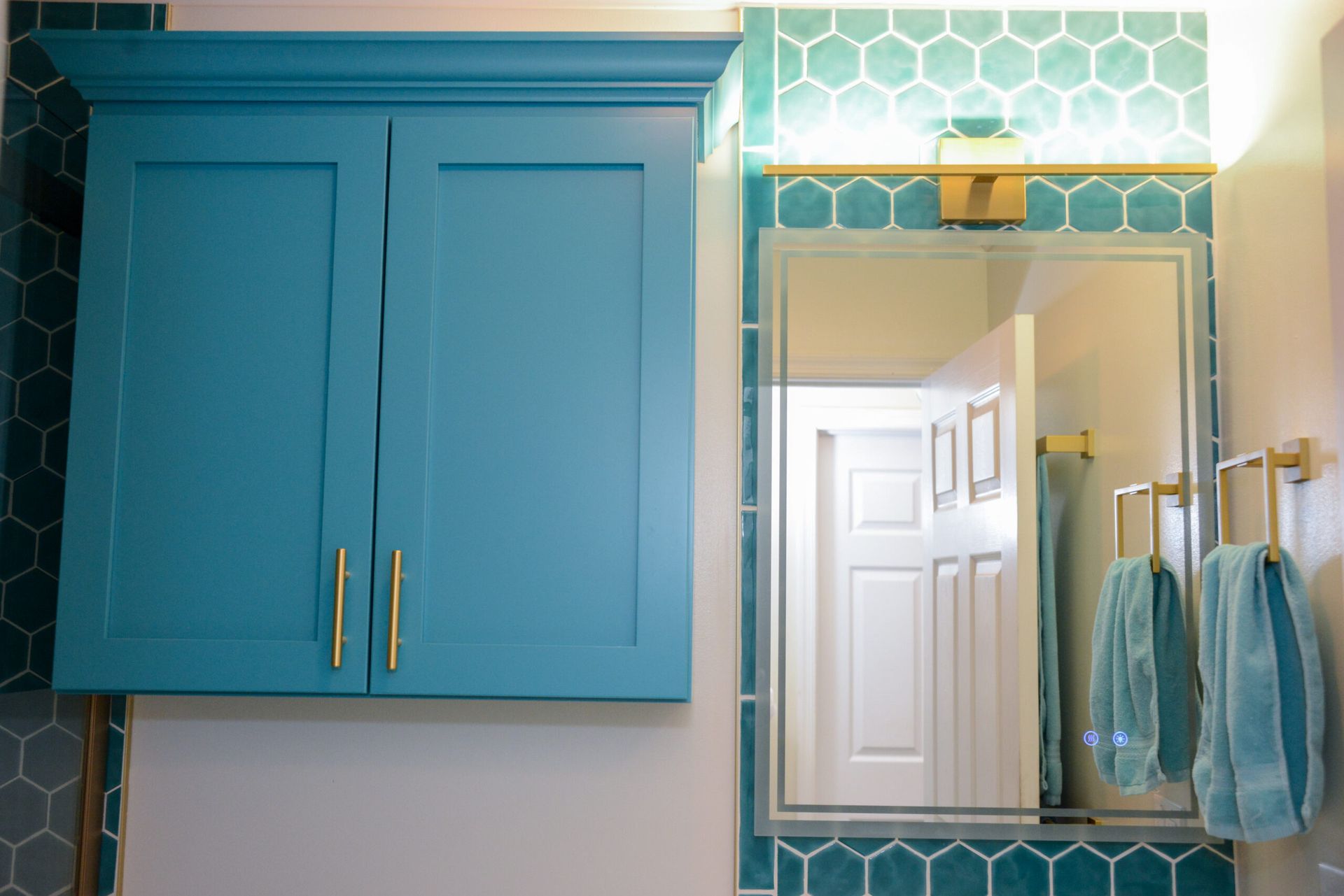 Teal bathroom cabinet and mirror with hexagon tile backsplash and gold fixtures