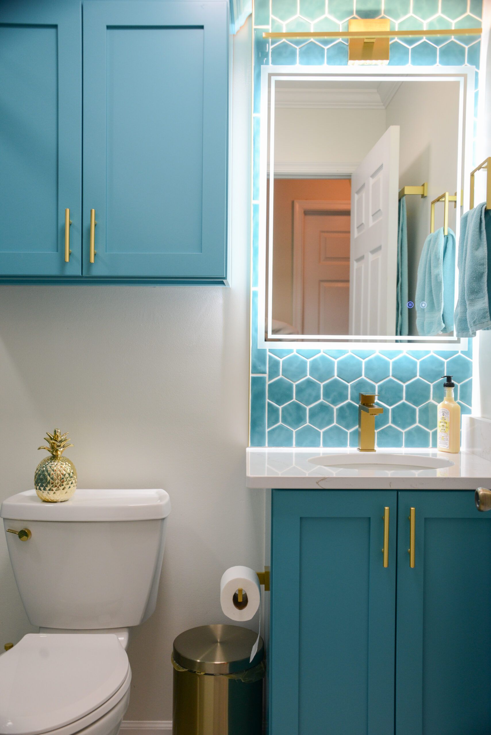 Teal bathroom with white vanity, gold fixtures, mirror, toilet, and patterned turquoise backsplash.