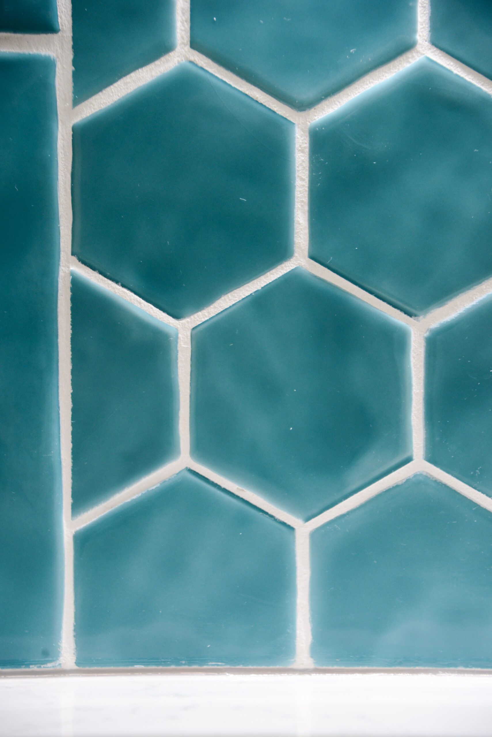 Teal hexagonal tile wall with white grout lines above a white baseboard