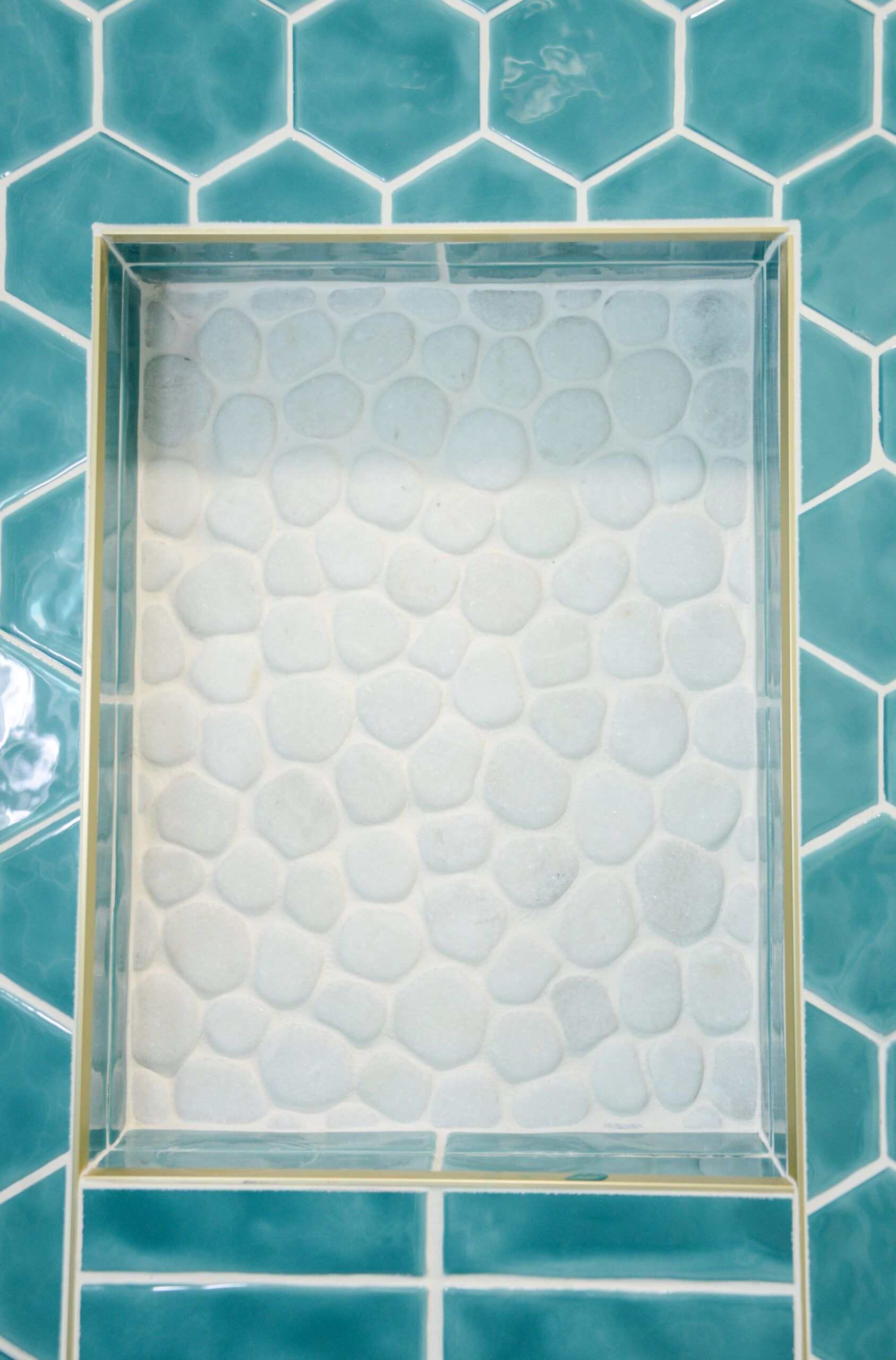 Rectangular tiled shower niche with turquoise and white hexagon tiles around a frosted glass center.