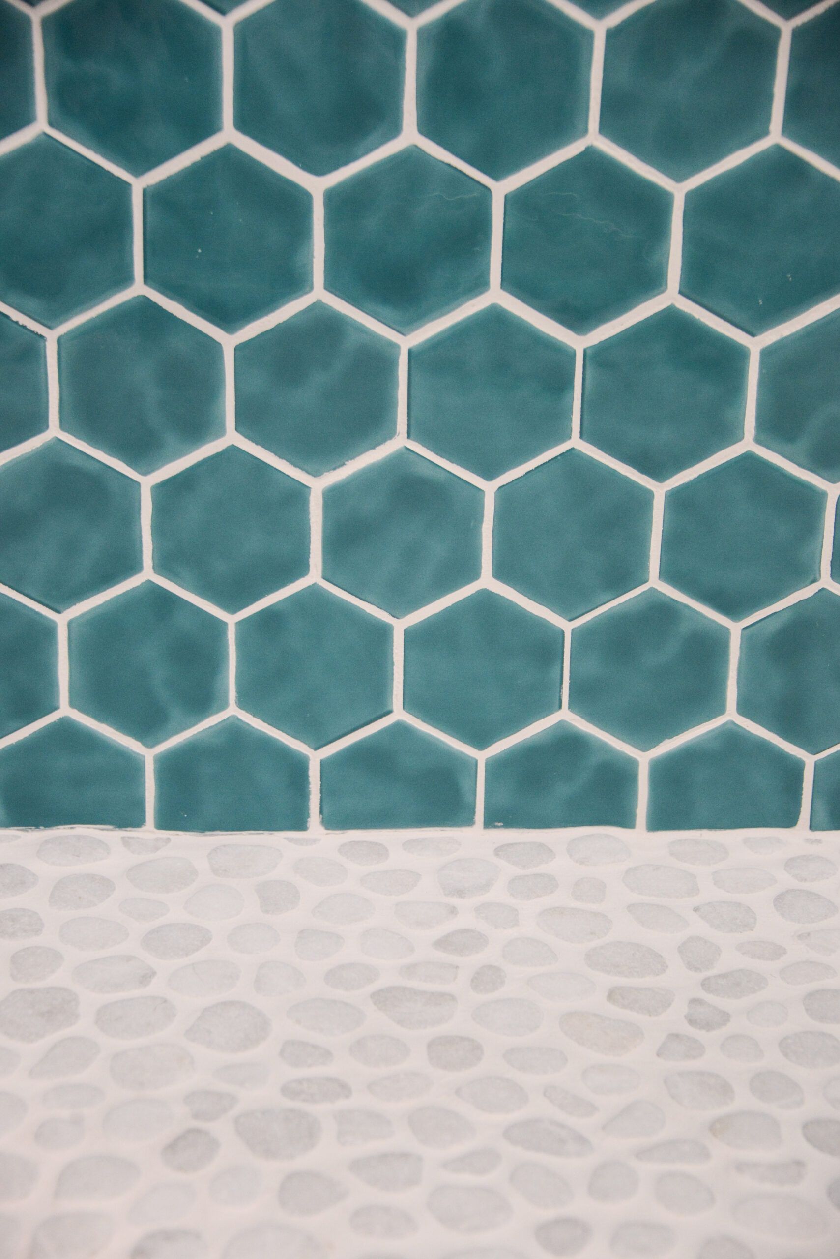Teal hexagonal tile wall above a white pebble-textured floor or countertop