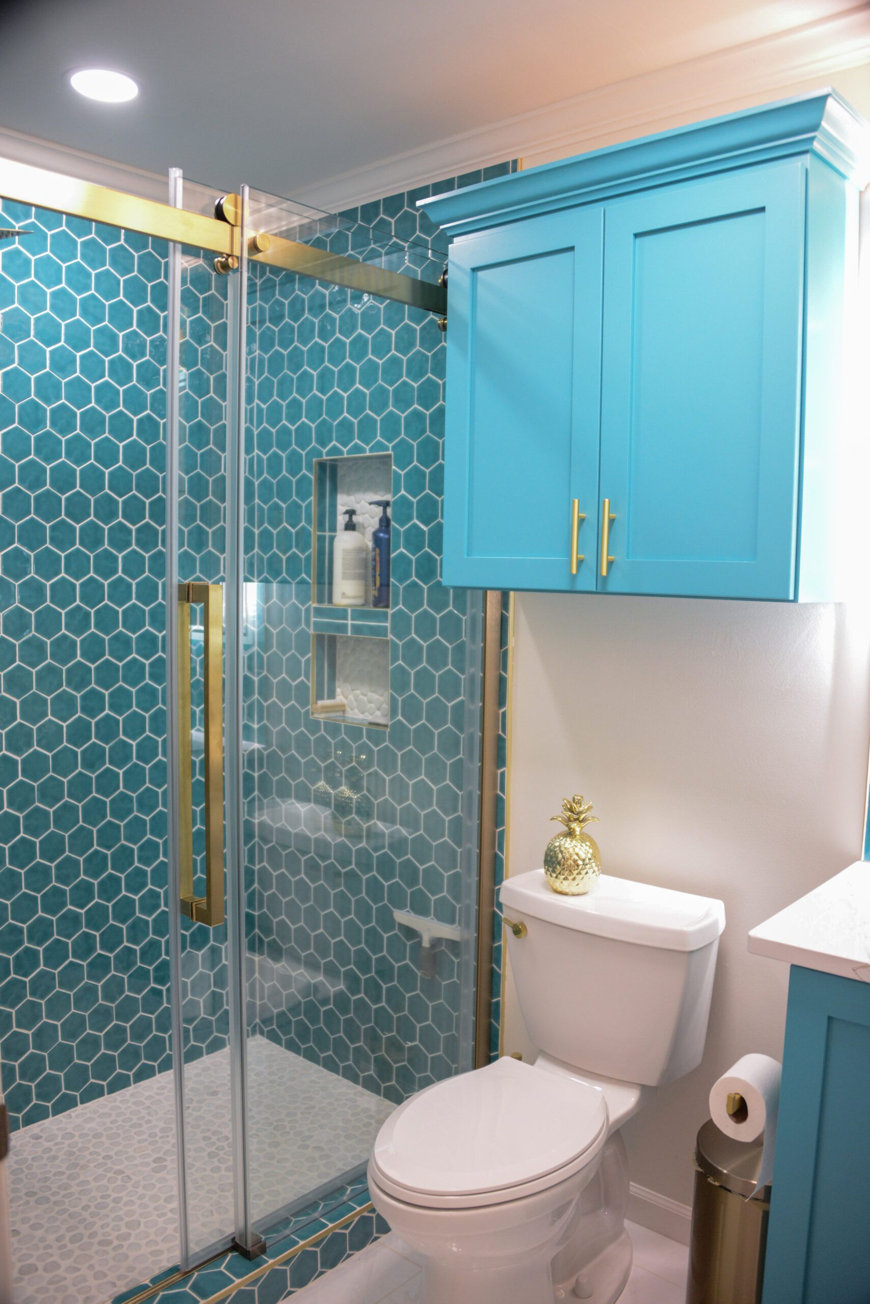 Teal-tiled bathroom with glass shower, white toilet, and turquoise cabinet over the toilet.