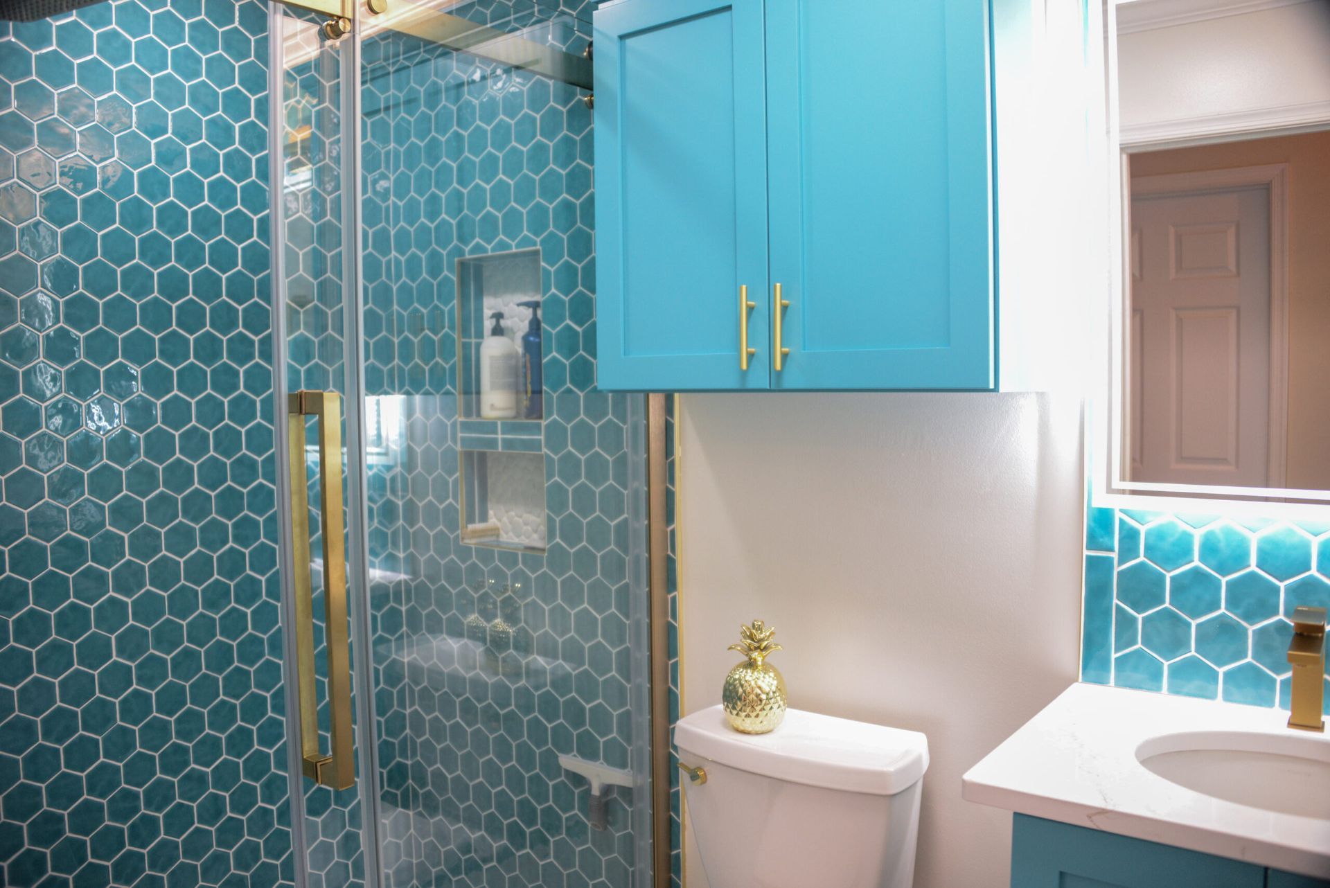 Teal tiled bathroom with glass shower, blue cabinets, white toilet, and vanity sink