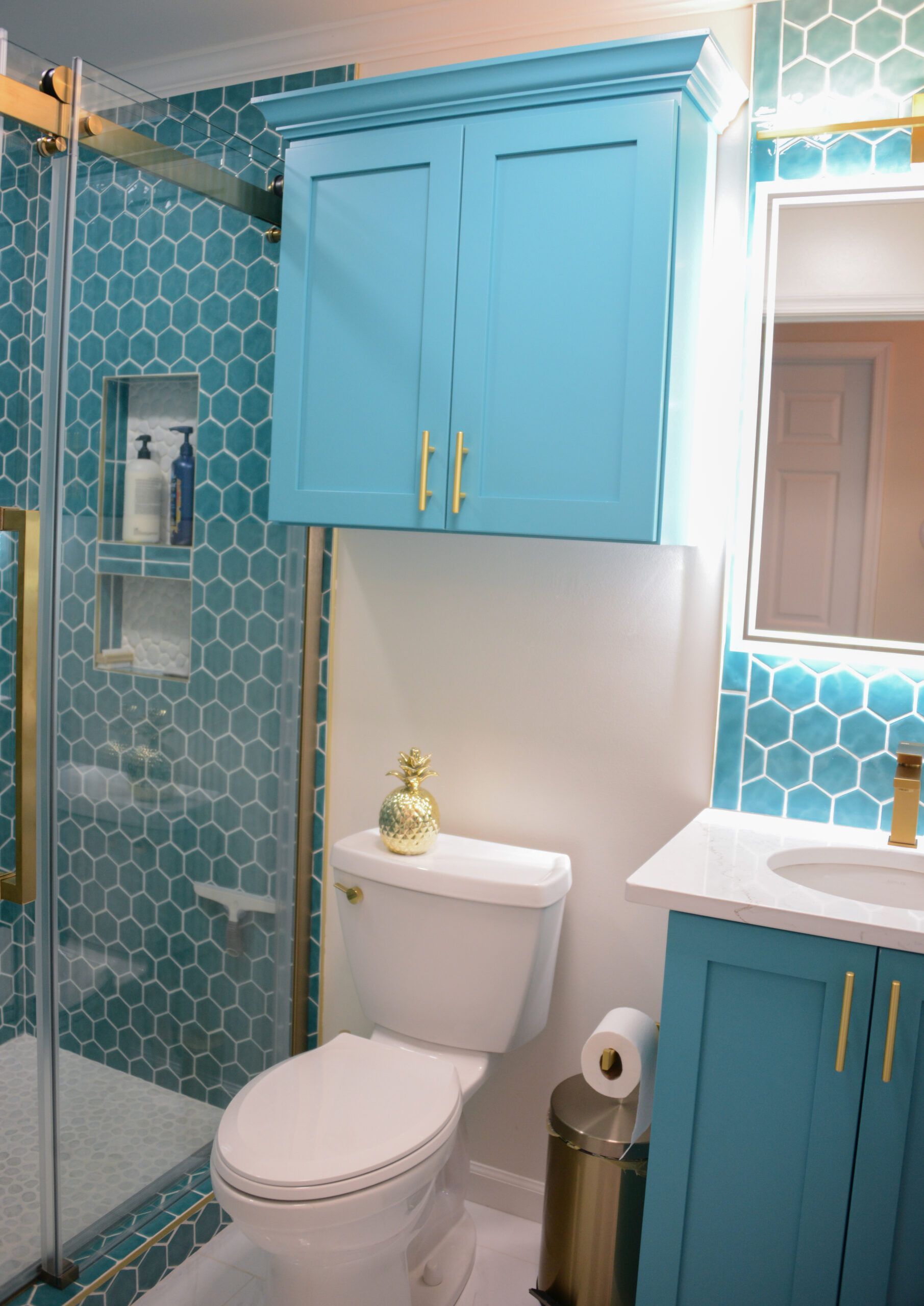 Blue-tiled bathroom with white toilet, teal cabinets, and a shower stall