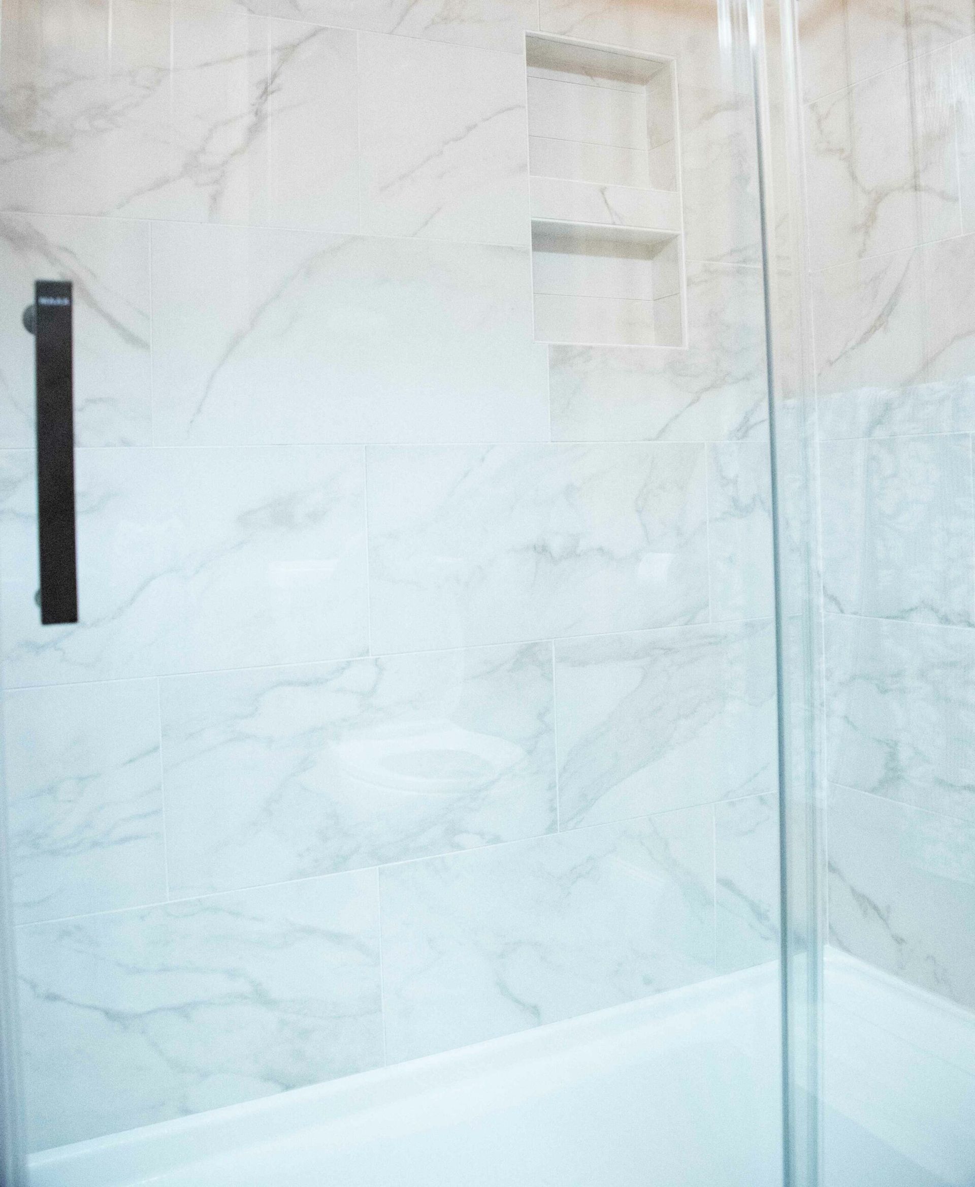 Modern white tiled shower with a glass door and black handle