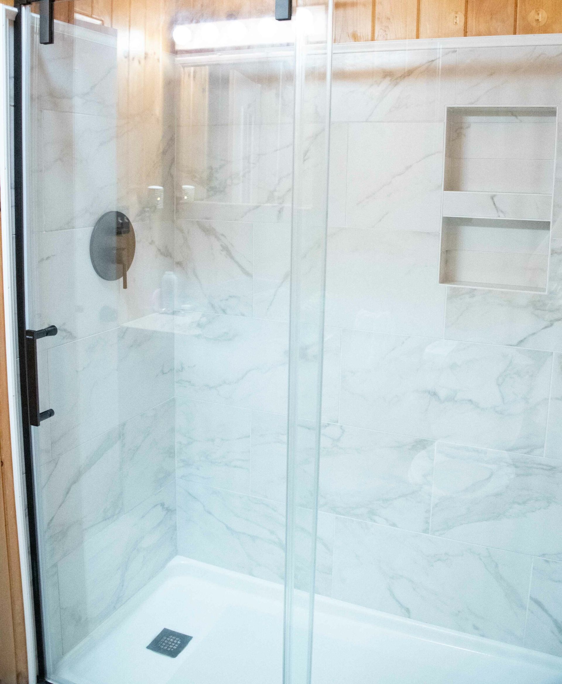 Glass walk-in shower with white tile walls and a small built-in shelf, viewed from outside the door
