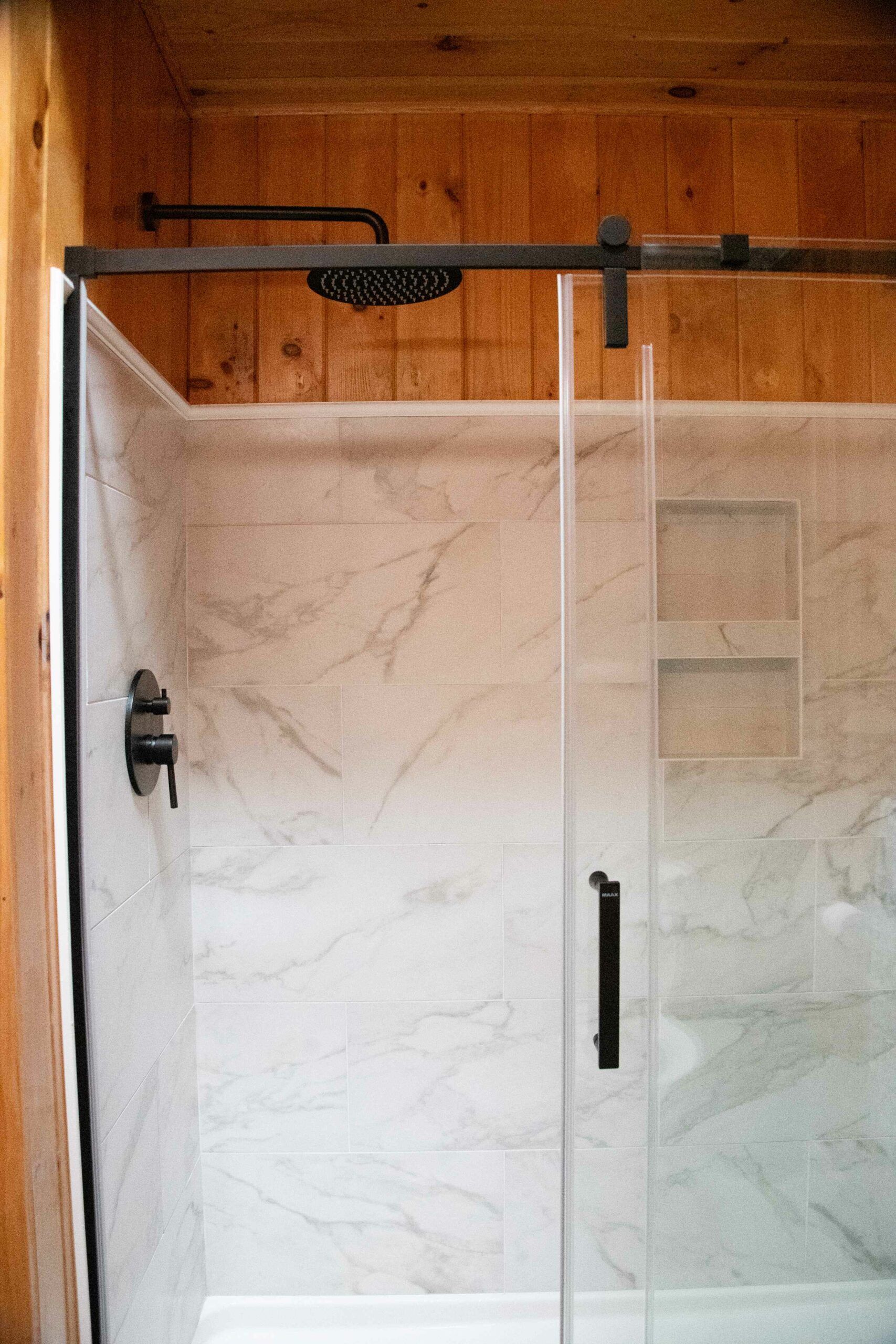 Glass shower enclosure with marble-look tile walls and a dark wood ceiling above