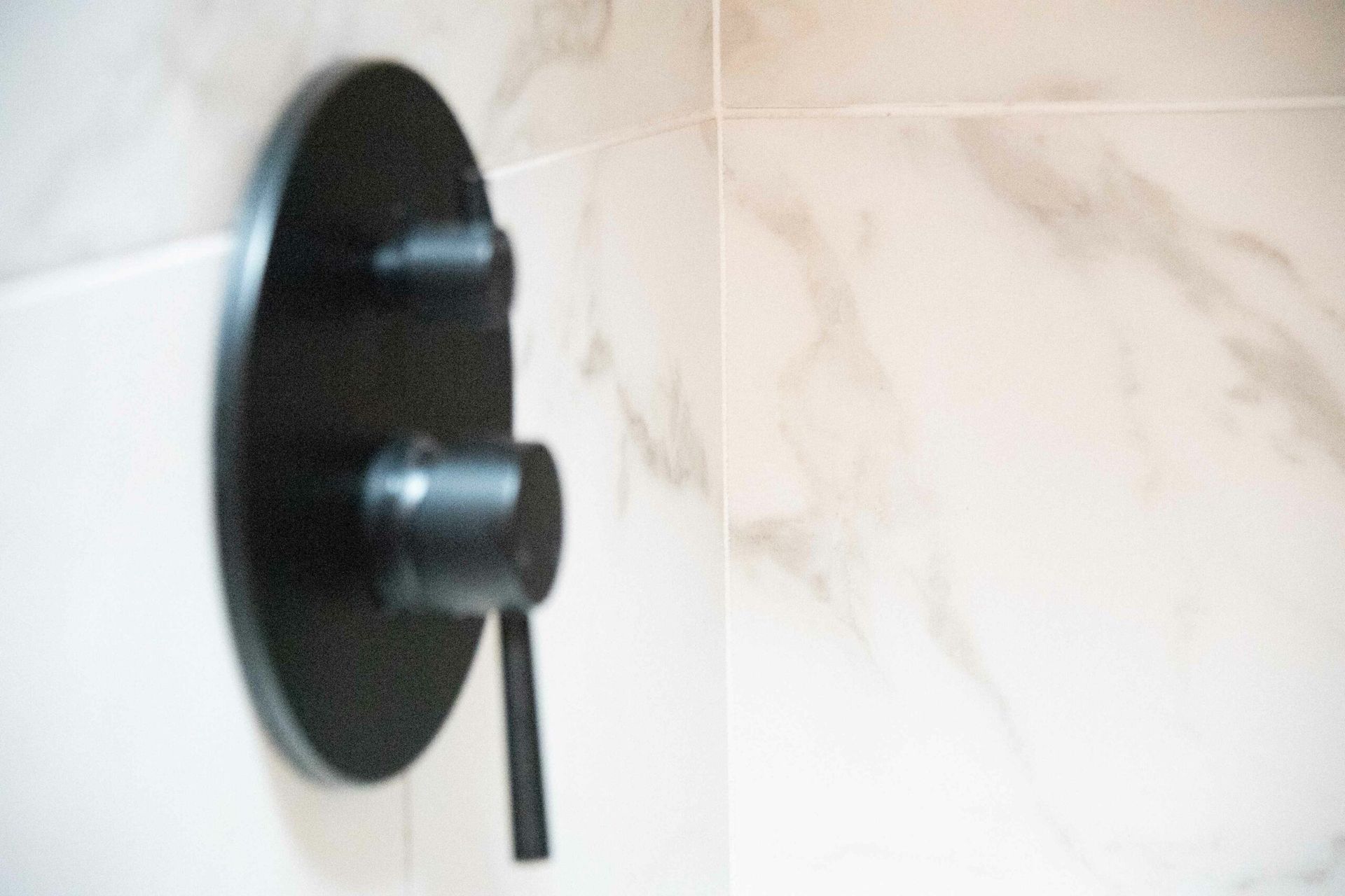 Black shower valve with handle on a tiled bathroom wall