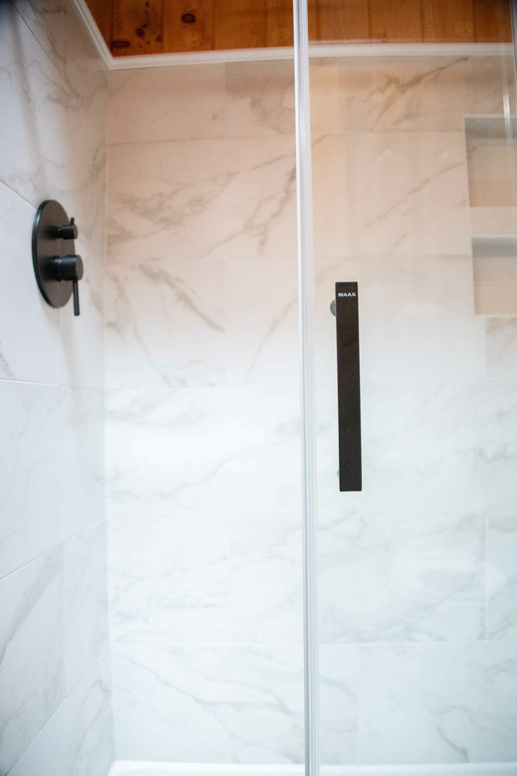 White tiled shower doors with black handles and a wooden trim at the top.