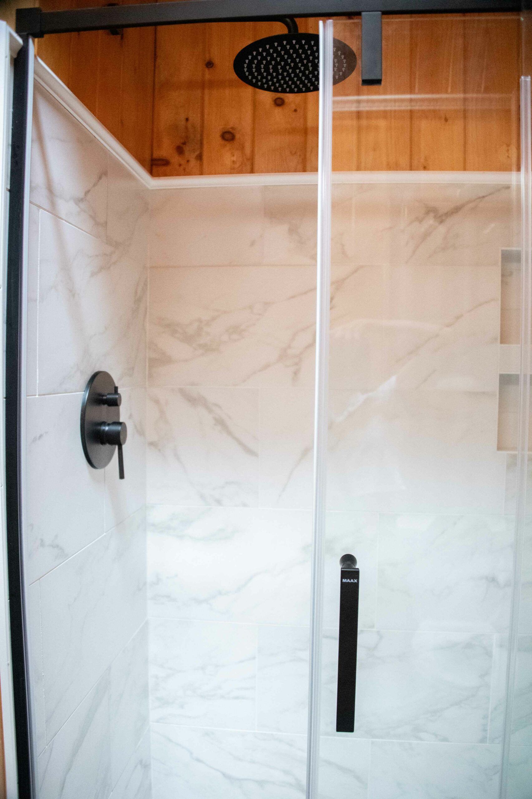 Glass shower enclosure with white tile walls and wood paneling above