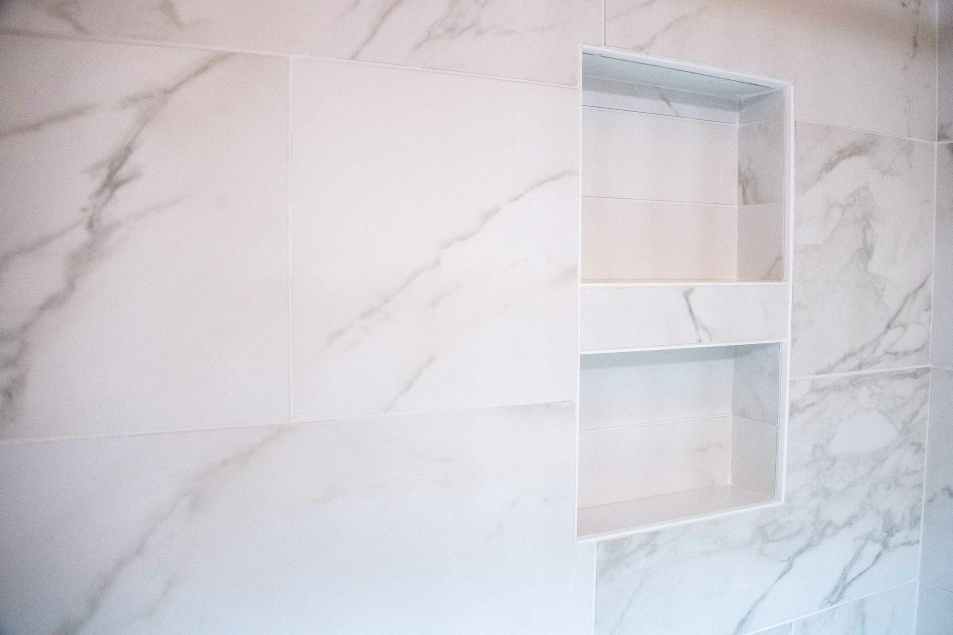 White marble-tiled shower wall with a recessed shelf niche
