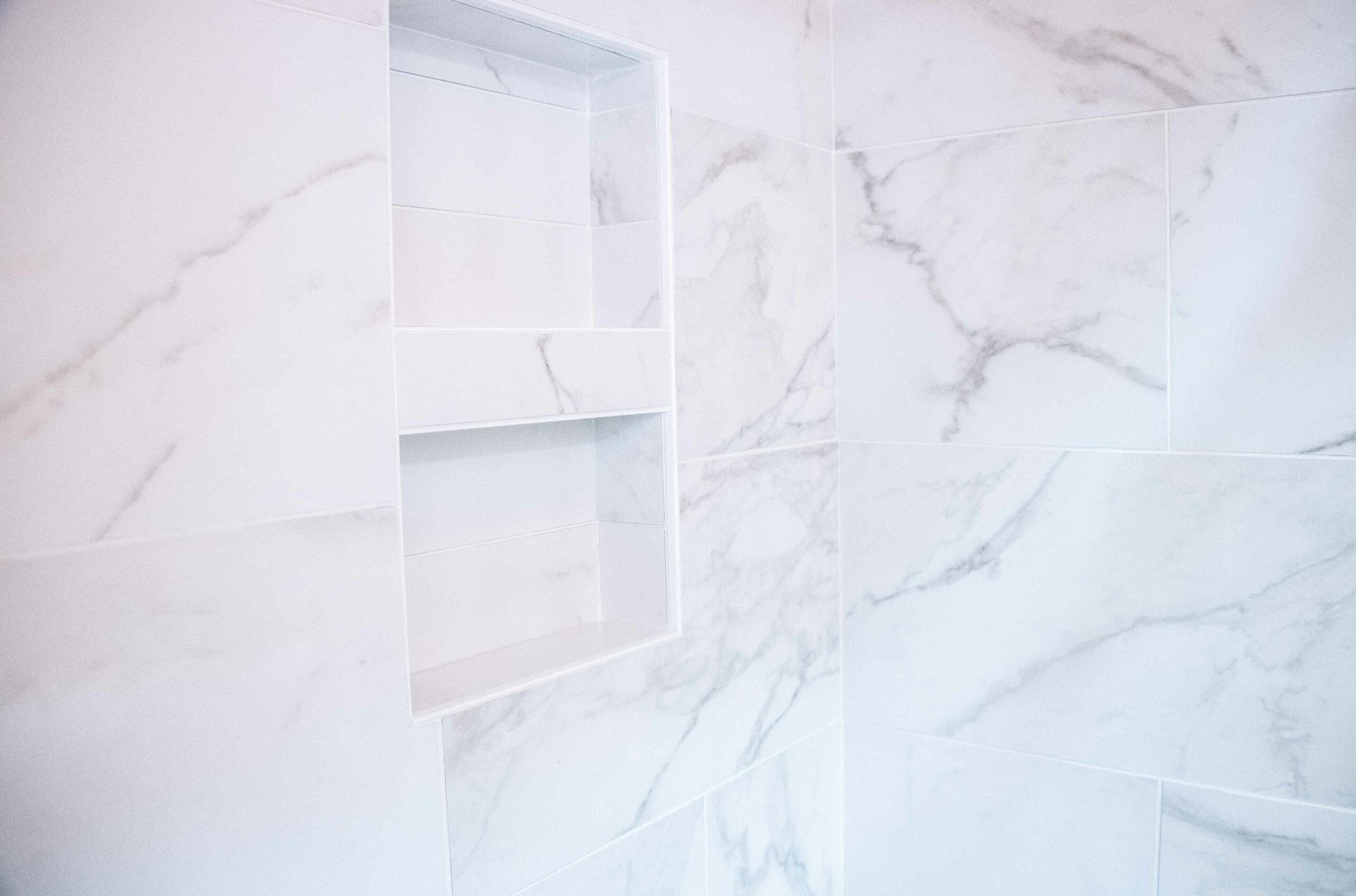 White marble bathroom wall with a recessed shelf and shower bench area