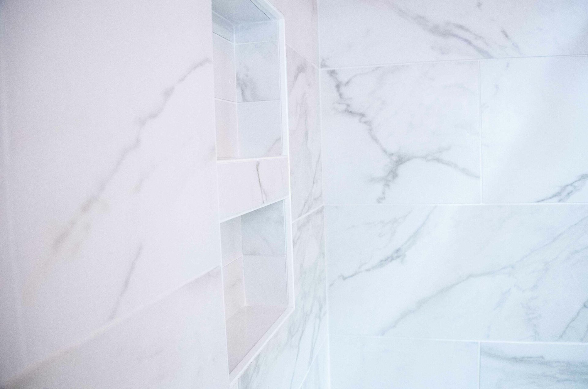 White marble-tiled shower wall with built-in corner shelf niches