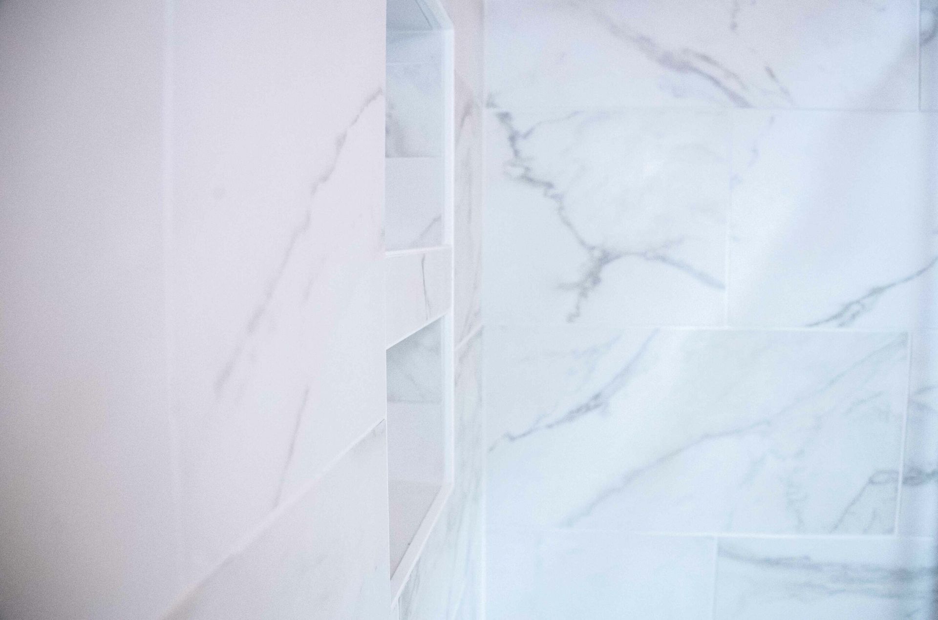 Bright white marble-tiled shower with a built-in niche shelf and glass door