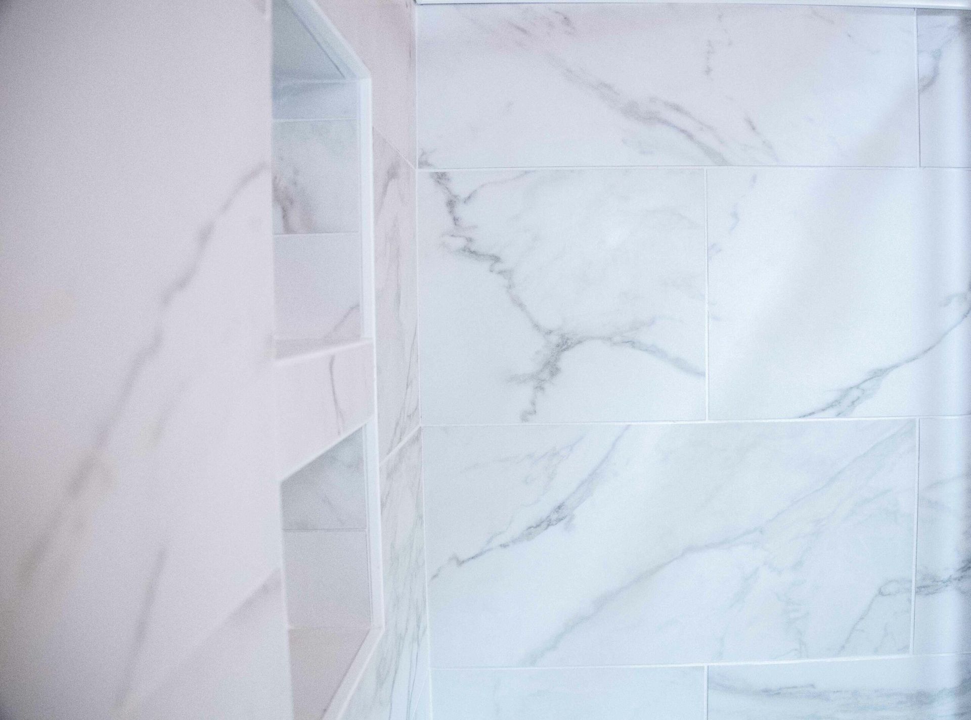 White marble-tiled shower wall with a small built-in niche shelf