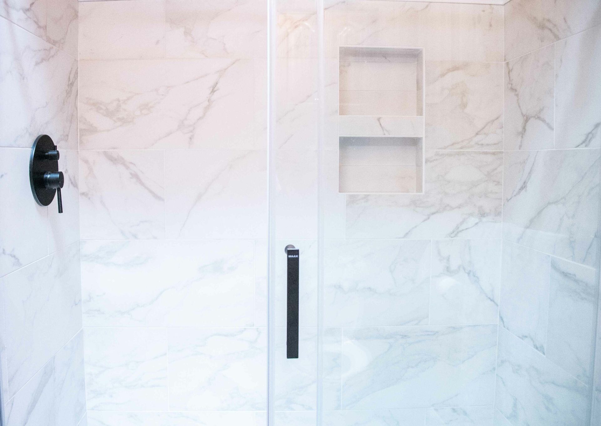 Sliding shower door with frosted glass, black handle, and recessed shelf in a marble-tiled bathroom