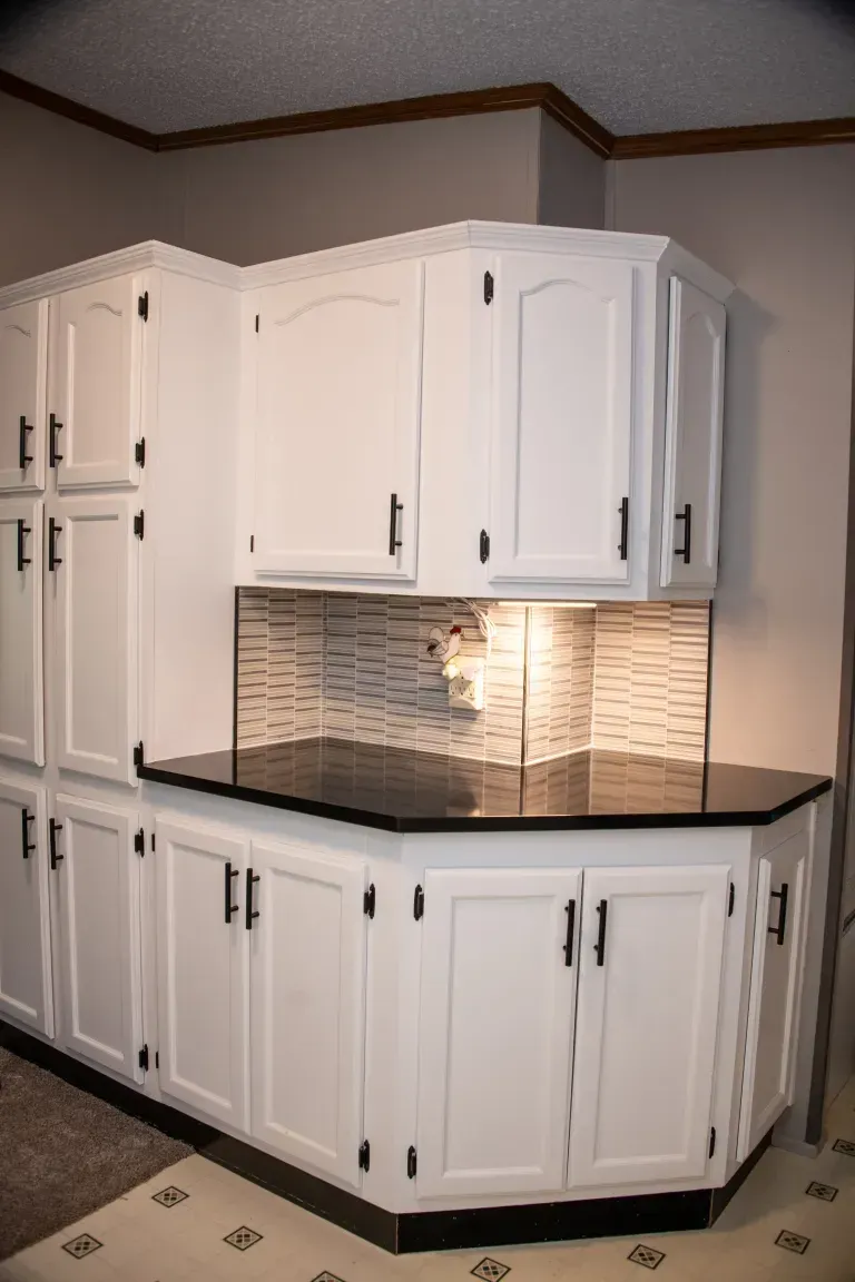 White kitchen corner with upper and lower cabinets, black countertops, and tiled backsplash.
