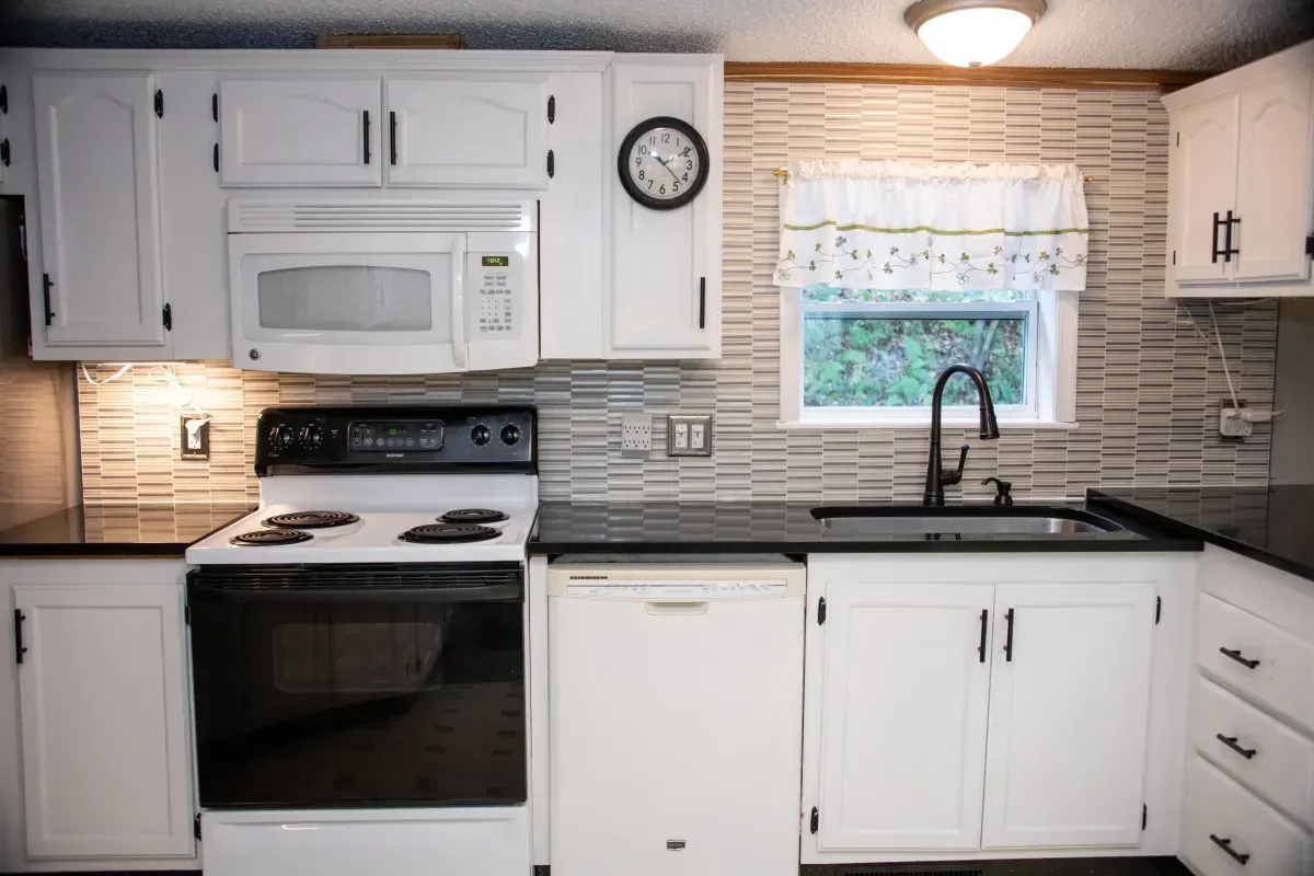 White kitchen with stove, microwave, sink, cabinets, and window above the counter.