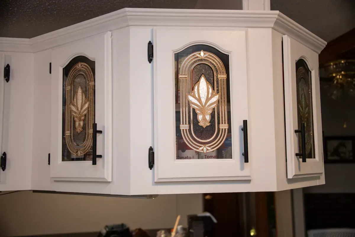 White kitchen cabinet with decorative black-and-gold glass door panels and black hinges
