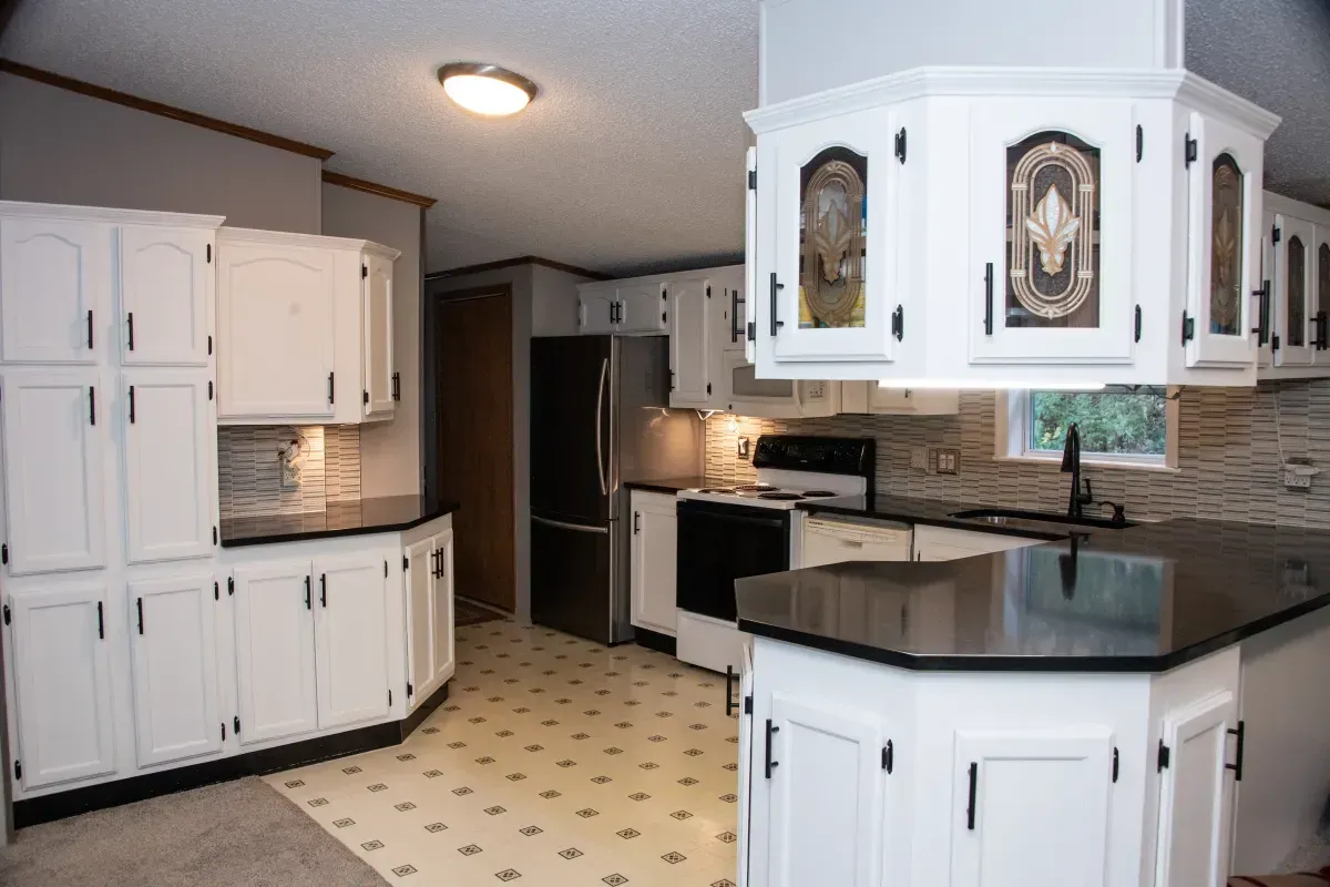 Bright white kitchen with black countertops, island, cabinets, and tiled floor
