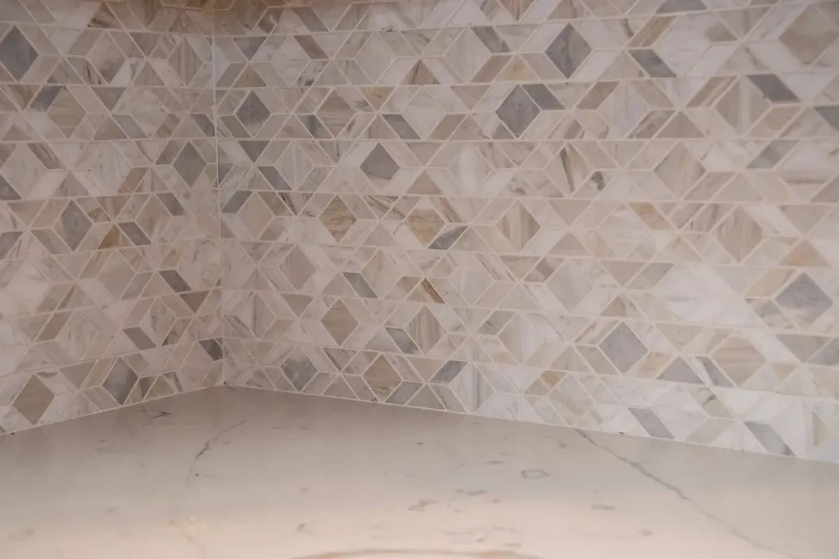 Empty tiled corner with beige geometric wall tiles and a light stone floor.