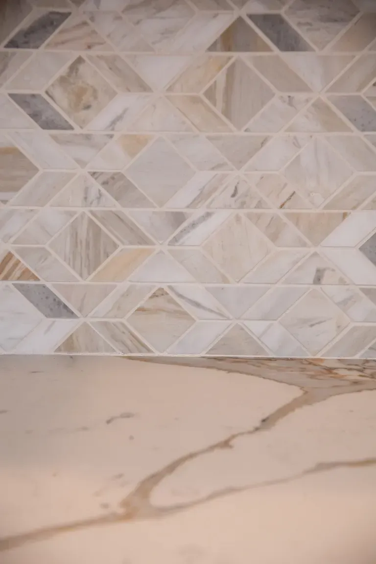 Beige geometric tile backsplash above a white marble countertop with gray veining