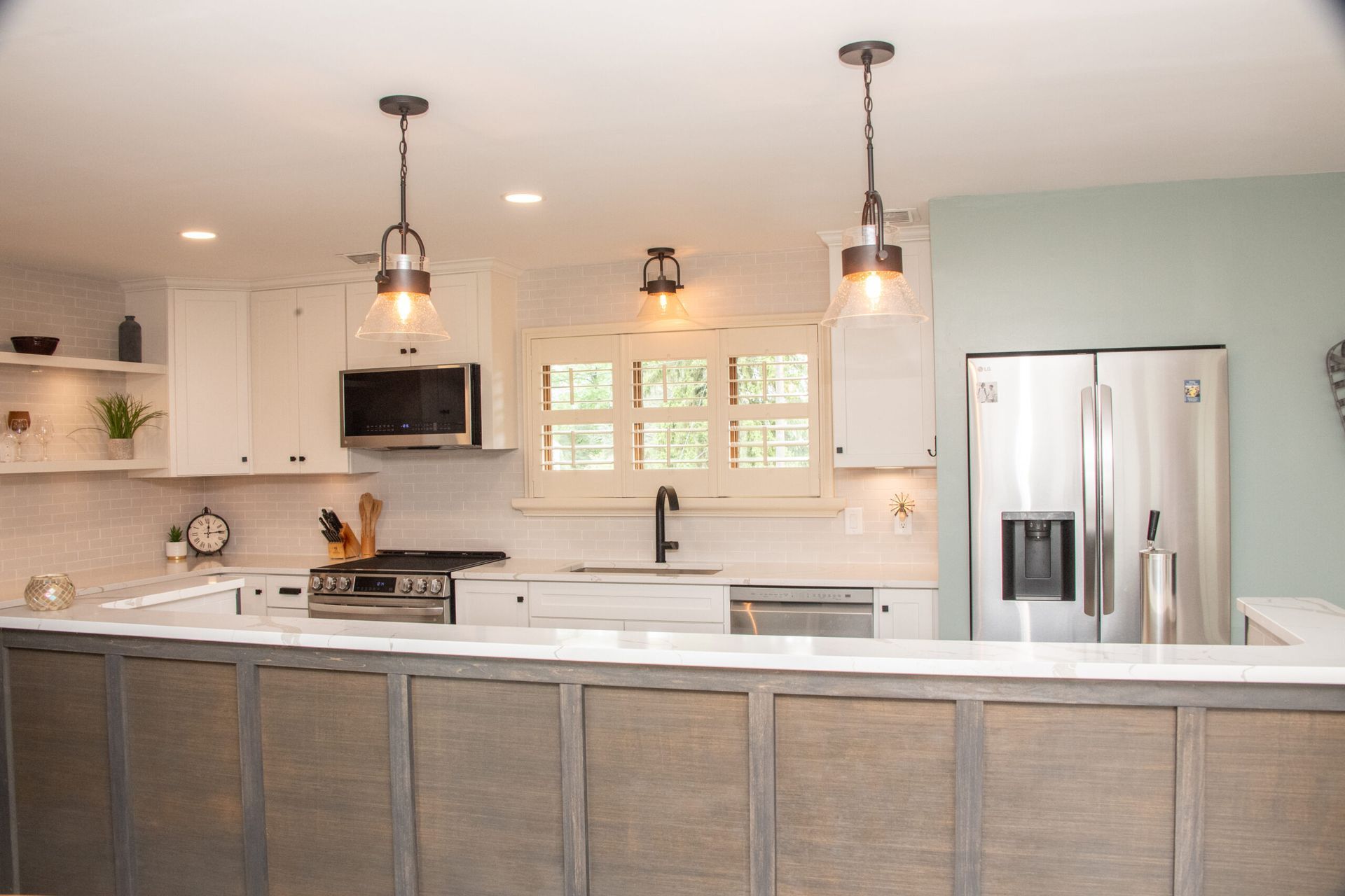 Bright modern kitchen with white cabinets, gray island, pendant lights, and stainless steel refrigerator.