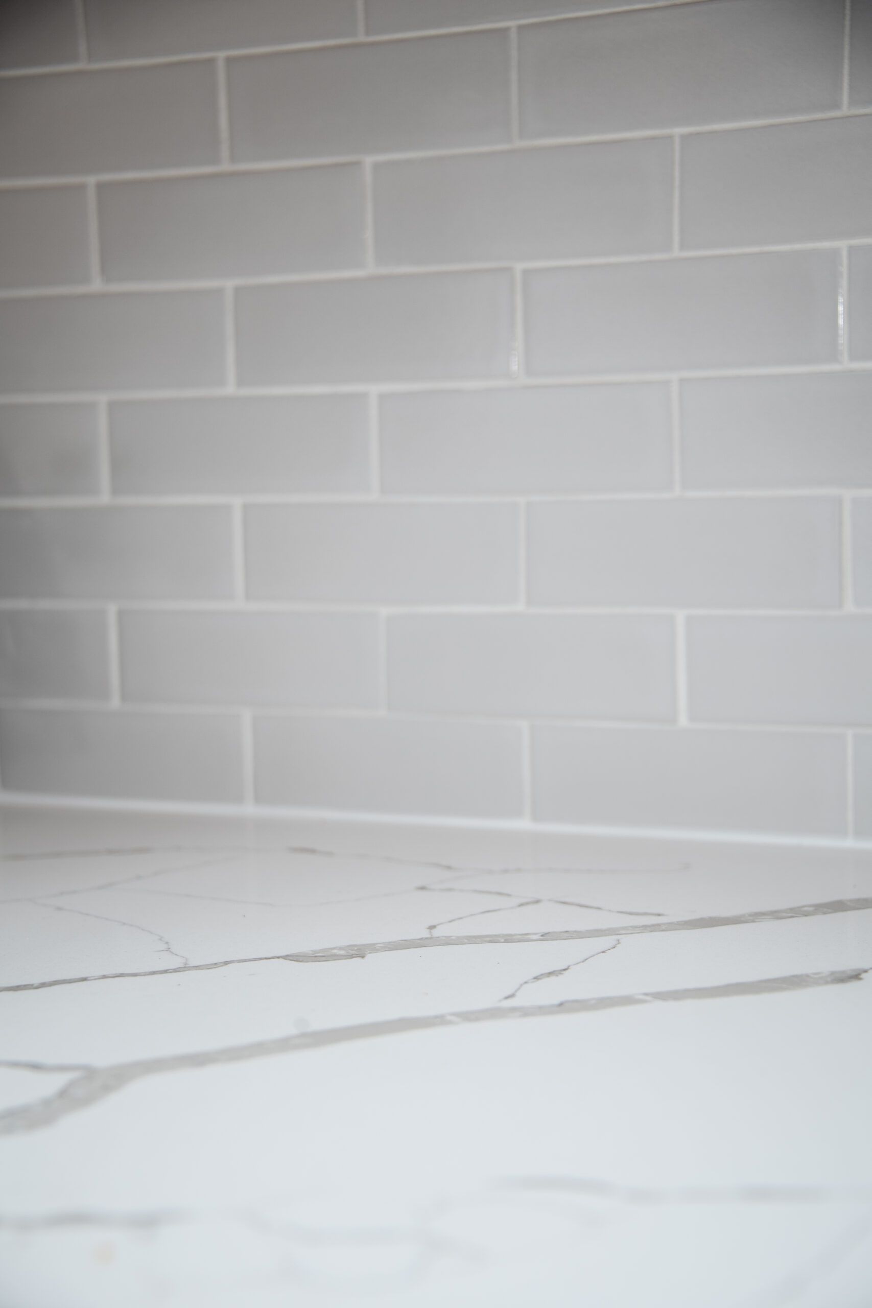 White tiled wall above a light marble countertop or floor with gray veining