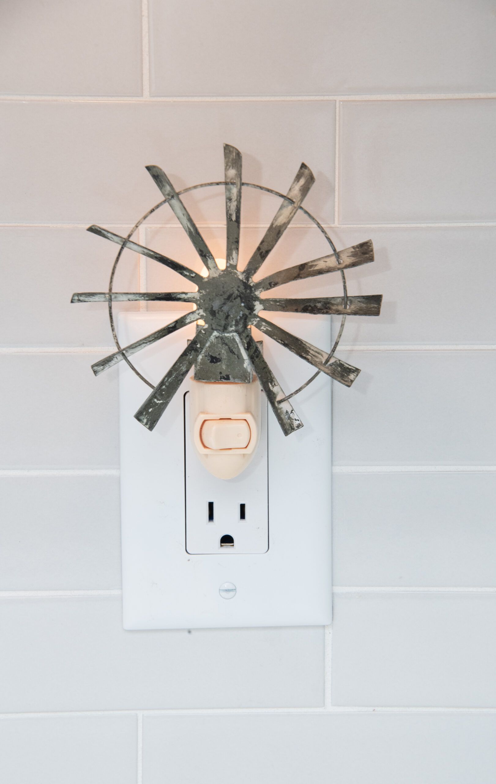 Wall outlet with a decorative fan-shaped metal cover on a white tiled wall