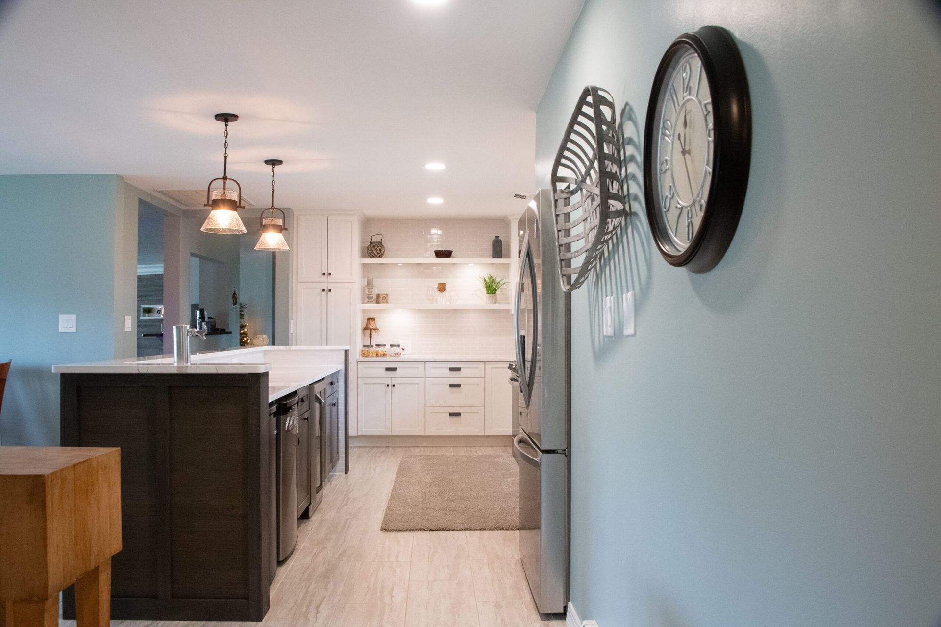 Modern kitchen and hallway with light blue walls, white cabinets, dark island, and large wall clock