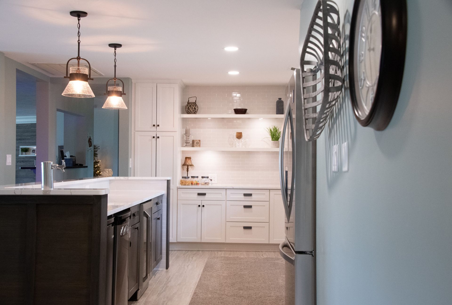Modern kitchen with white cabinets, marble island, pendant lights, and a wall clock on a blue wall
