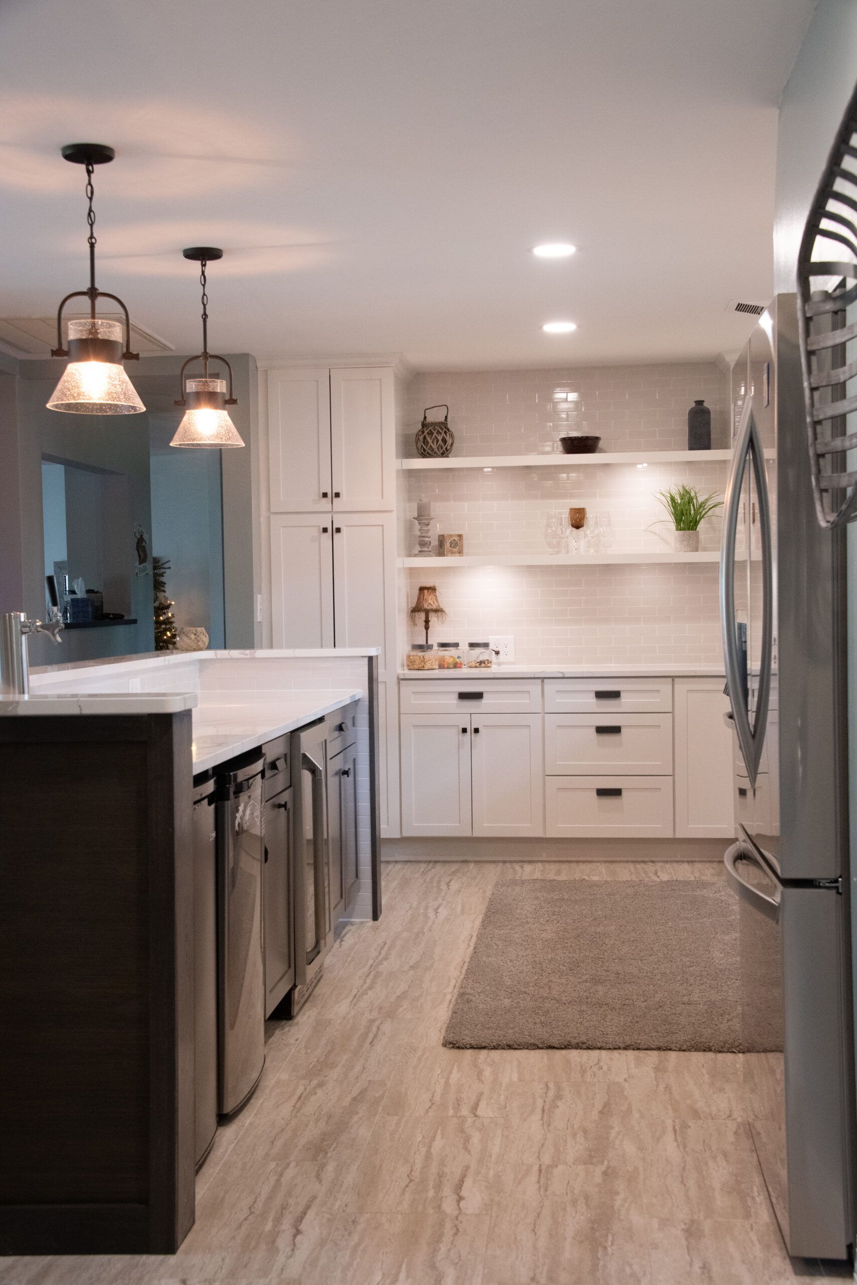 Bright modern kitchen with white cabinets, island stools, pendant lights, and stainless steel fridge