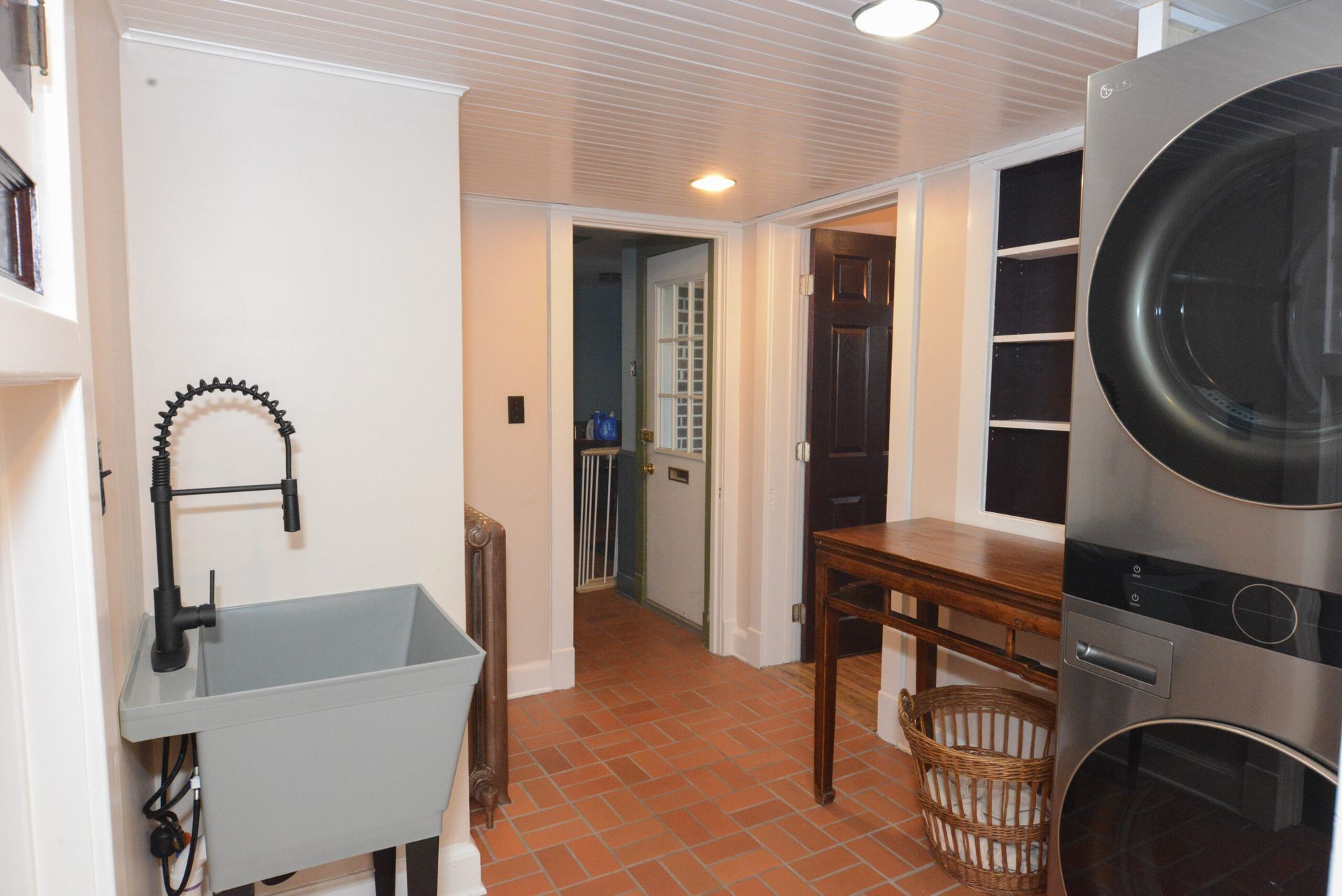 Laundry room with sink, tiled floor, wooden table, and stacked washer and dryer