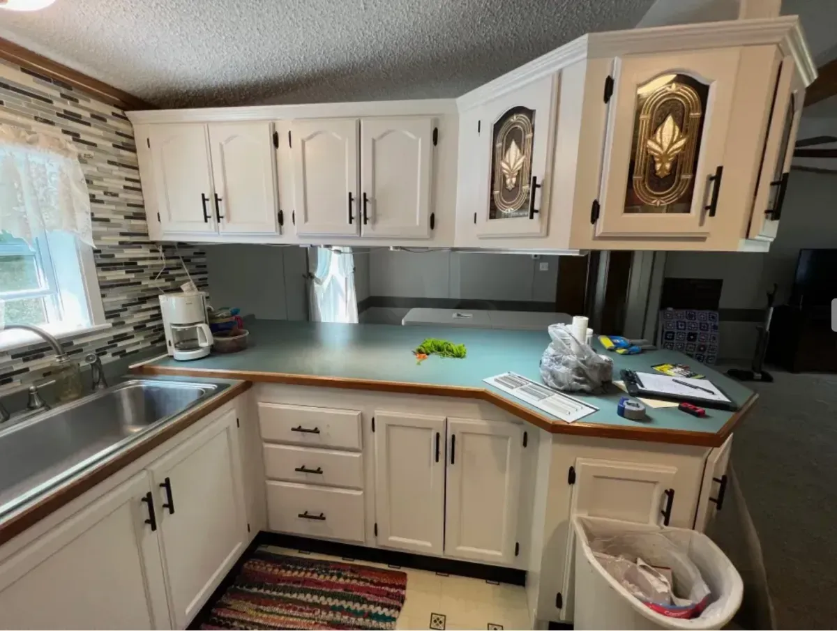Small kitchen with white cabinets, gray countertop, sink, window, and a colorful rug on the floor.