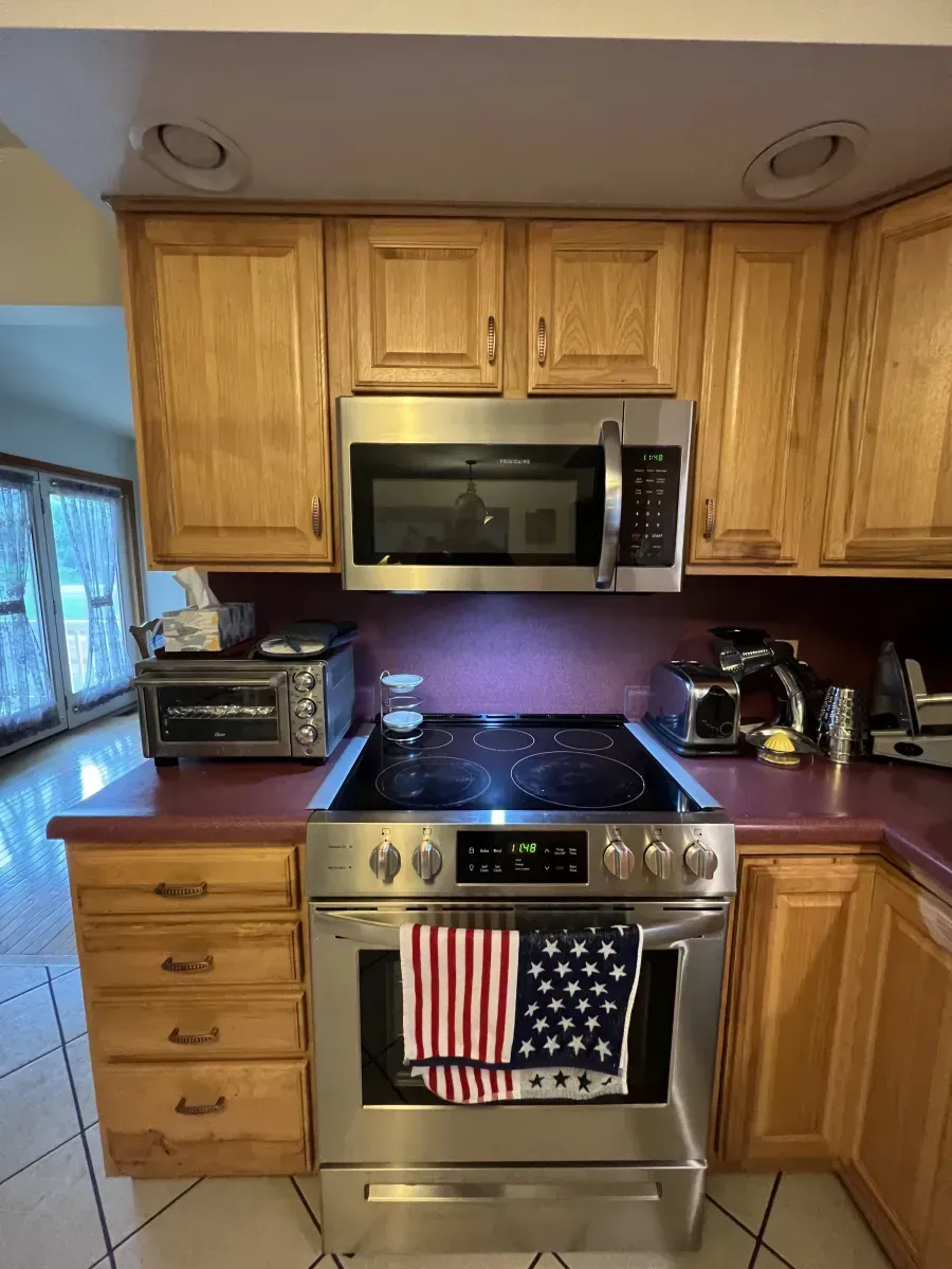 Kitchen with stainless steel stove and microwave, honey oak cabinets, purple backsplash, and a toaster oven on the counter