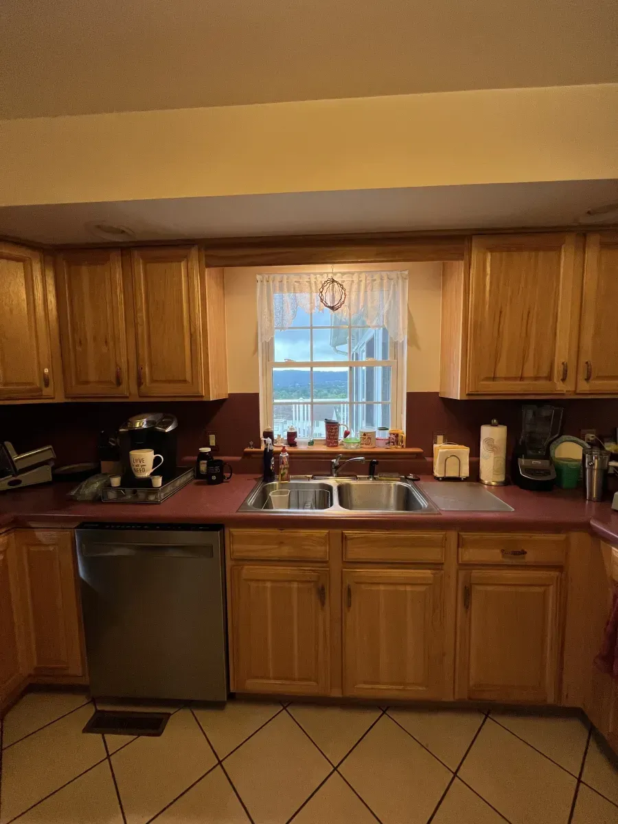Kitchen with wooden cabinets, tiled floor, sink under a window with curtains, and countertop appliances.